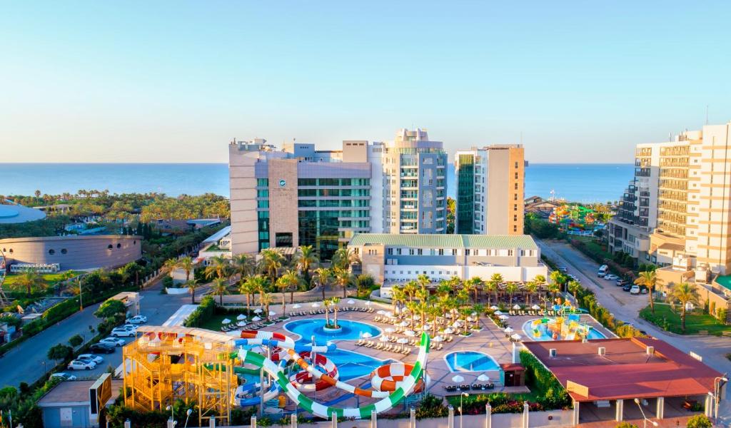 Exterior view of Sherwood Exclusive Lara Resort in Antalya, featuring its main building, outdoor pools, water slides, and proximity to the beachfront.