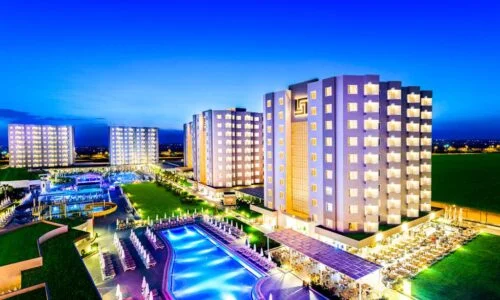 Night view of the Grand Park Lara Hotel Antalya, showcasing its illuminated modern architecture, expansive pool area, and vibrant resort atmosphere.